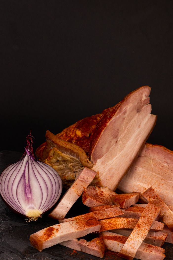 Close-up of smoked ham slices and a red onion on a dark background.